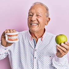 a senior man holding an apple and his dentures