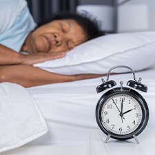 a woman sleeping in bed with a clock on her nightstand