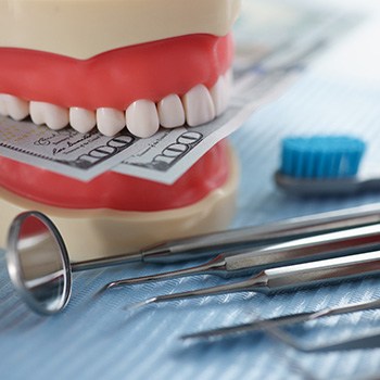 An artificial jaw mockup biting a couple hundred-dollar bills next to dental tools