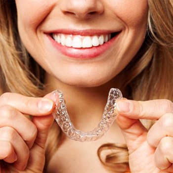 a woman smiling and holding an Invisalign tray