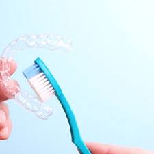 a person holding an Invisalign aligner and a toothbrush