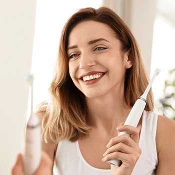 Smiling woman holding mechanical toothbrush after completing at-home oral hygiene routine
