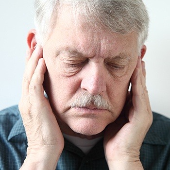 Older man with TMJ dysfunction holding jaw joints