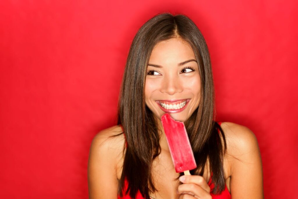 A woman eating a red popsicle.