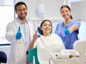 Patient, dentist, and hygienist all giving thumbs up and smiling